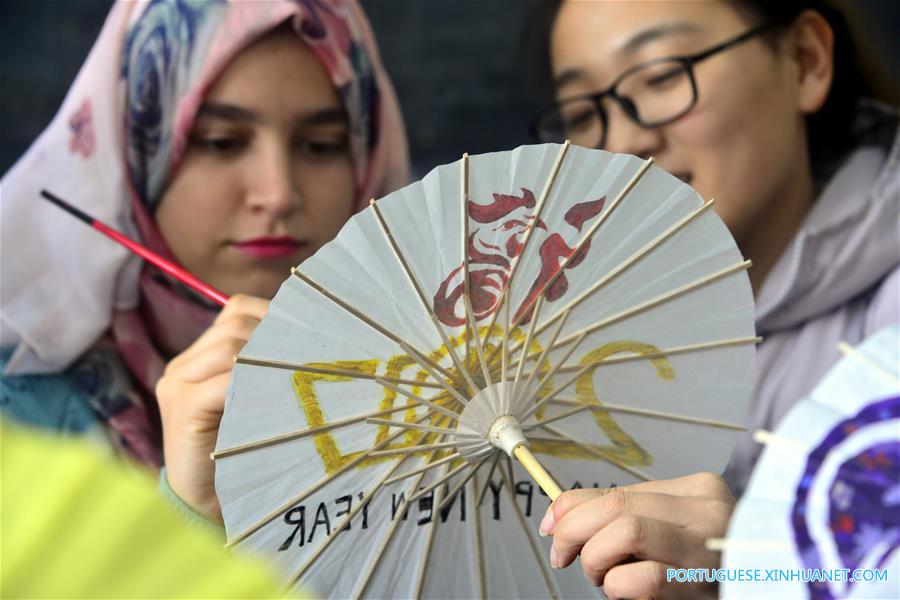 Estudantes internacionais pintam temas de galo em sombrinhas de papel chinesas